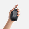 A hand is holding a black cooling towel with a mesh texture and a metal clip.