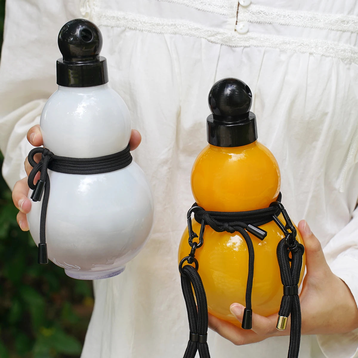 Eine Hand hält eine krugförmige Sportflasche in orange Farbe mit einem schwarzen Trageriemen.