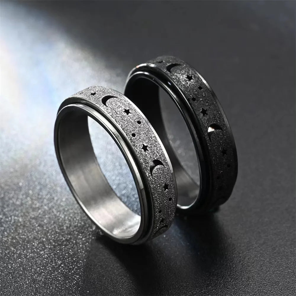 A pair of black stainless steel spinning rings featuring a moon and star design, resting on a dark surface.