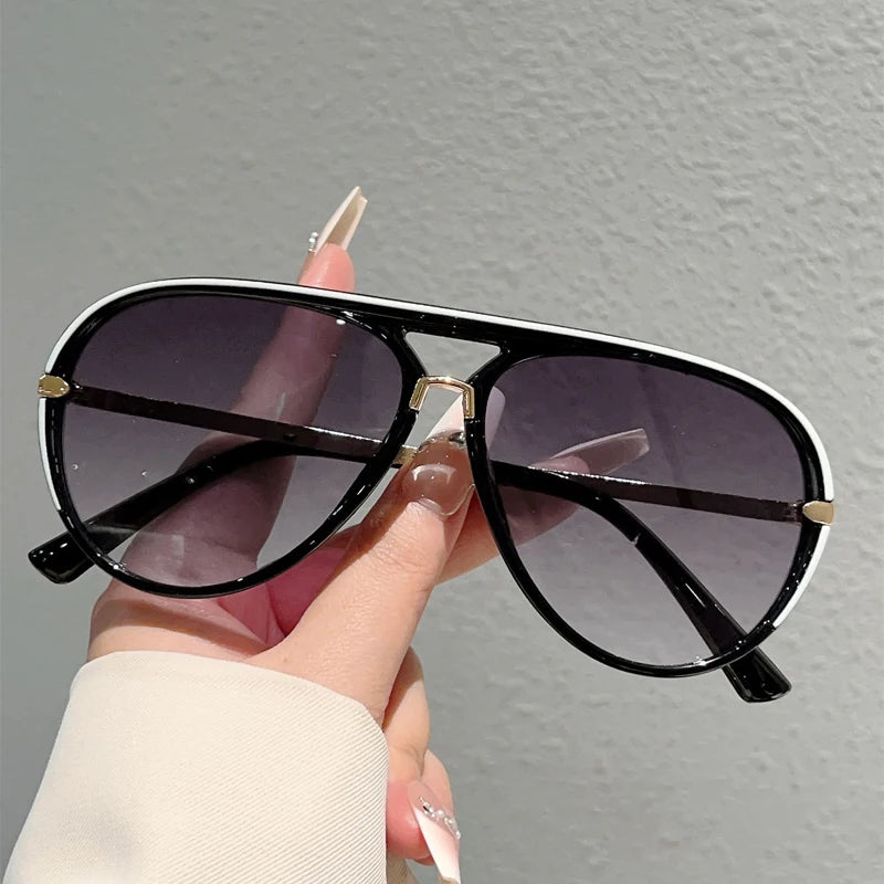 A hand holds a pair of black and white gradient sunglasses against a gray background.