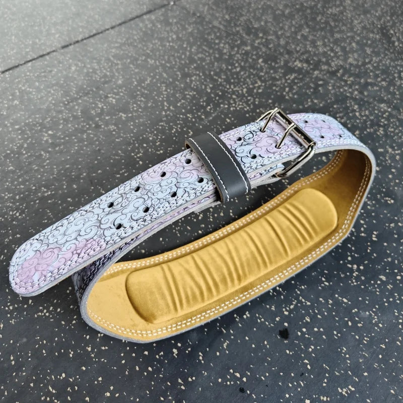 A light pink and white patterned leather weightlifting belt with a black buckle resting on a dark surface.
