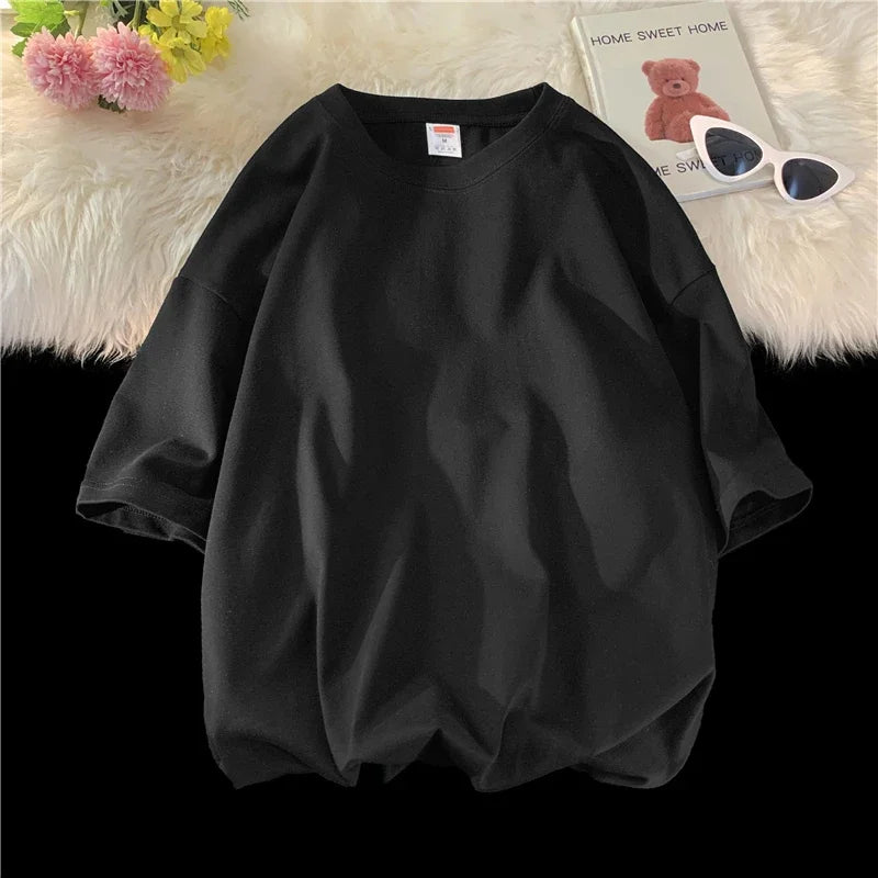 Schwarzes, überdimensioniertes Baumwoll-T-Shirt einer Frau, flach auf einer weißen, flauschigen Oberfläche.