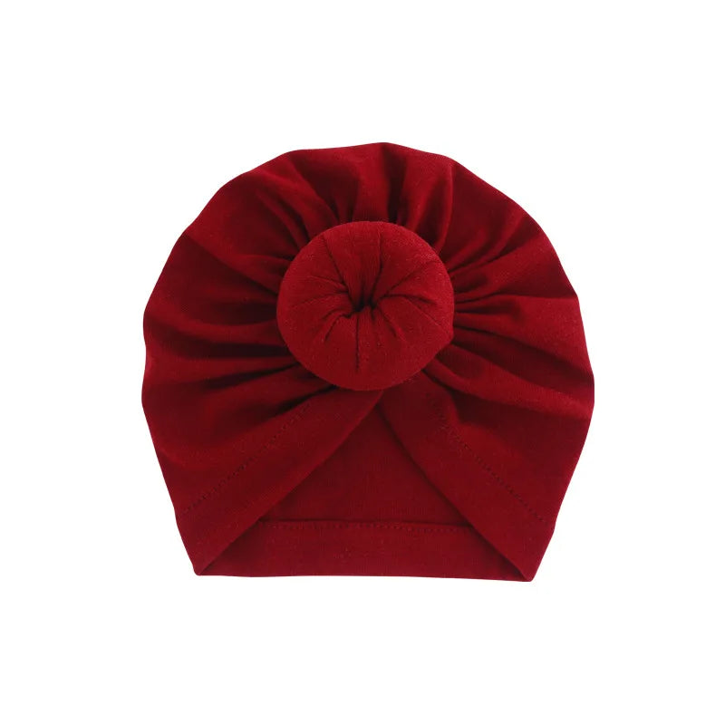 Tiefrote, solide Baumwoll-Baby-Turban-Kopftuch in Rosettenform gefaltet.