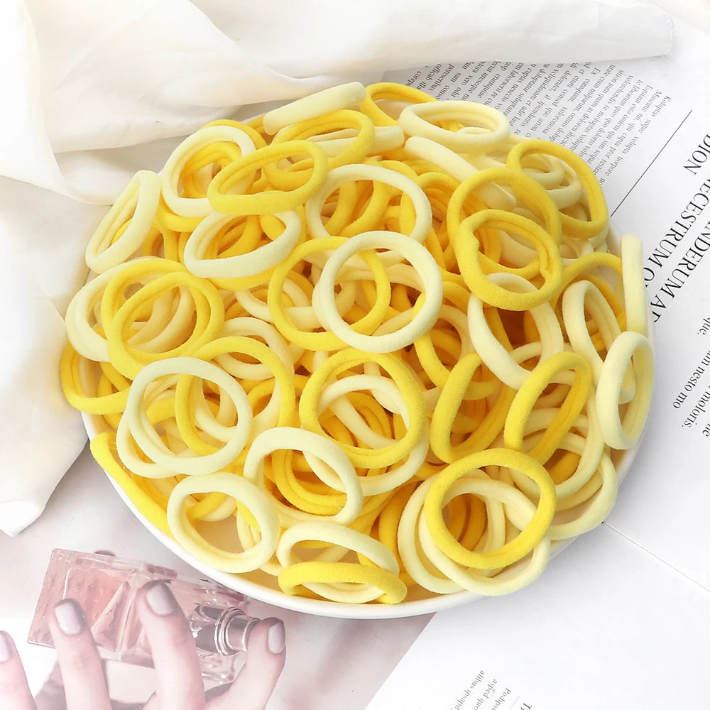 A pile of 50 elastic hair bands in mixed yellow and white colors arranged on a white surface.