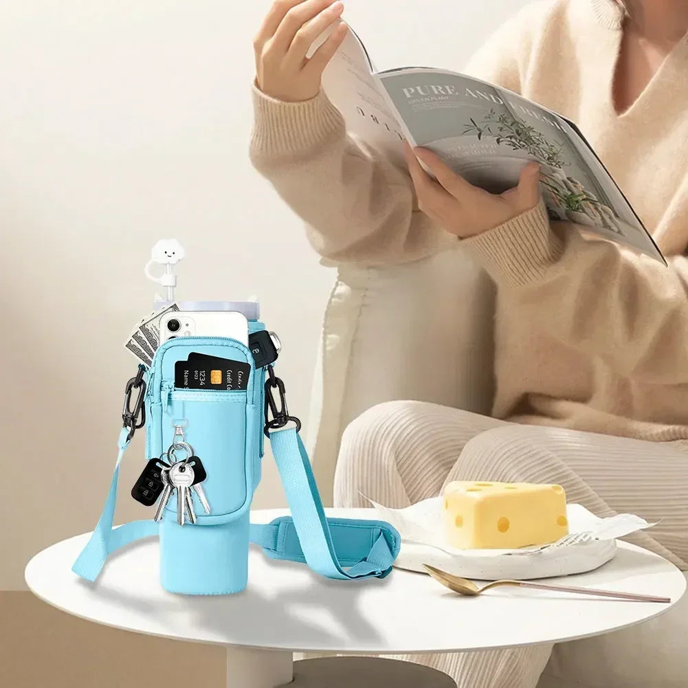 A light blue neoprene water bottle carrier bag with a strap is shown next to a book and food on a white table.