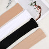 A pair of black and beige opaque thigh high elastic socks laid out on a white surface with a green leaf.