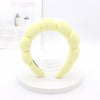 A yellow sponge terry cloth headband for hair styling displayed on a white circular stand.