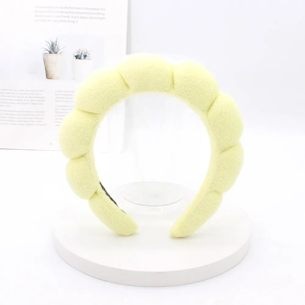 A yellow sponge terry cloth headband for hair styling displayed on a white circular stand.