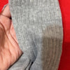 Una mano sostiene un par de calcetines de punto grises hasta la pantorrilla contra un fondo rojo.
