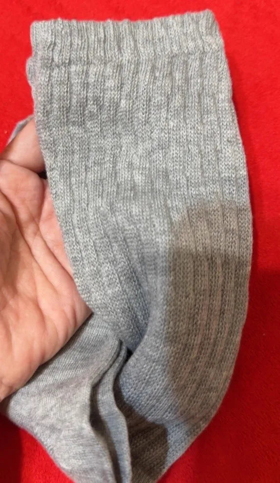 Una mano sostiene un par de calcetines de punto grises hasta la pantorrilla contra un fondo rojo.
