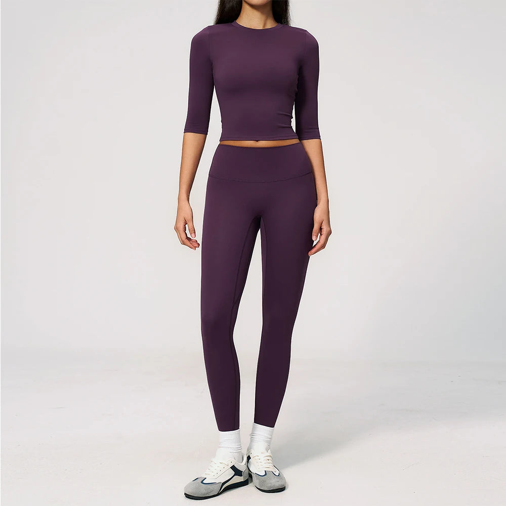 A woman wearing a matching purple yoga and fitness leggings set, consisting of a long-sleeved top and full-length pants.