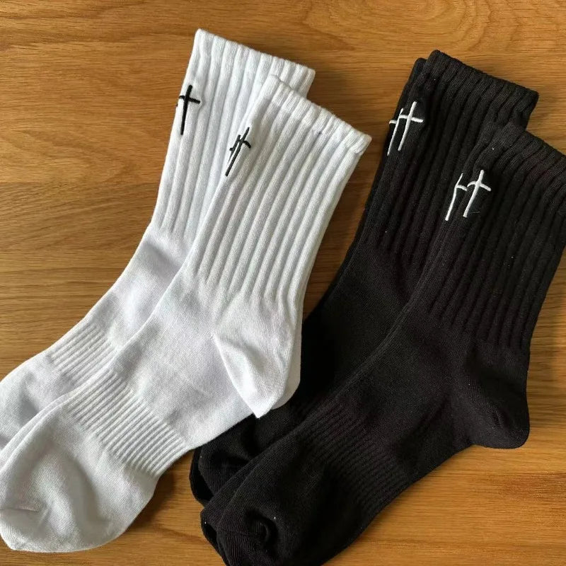A pair of white and black ribbed socks with a cross pattern laid out on a wooden surface.