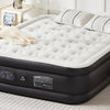 A black air mattress with a white quilted top and a beige towel is placed on a light-colored rug in a room.