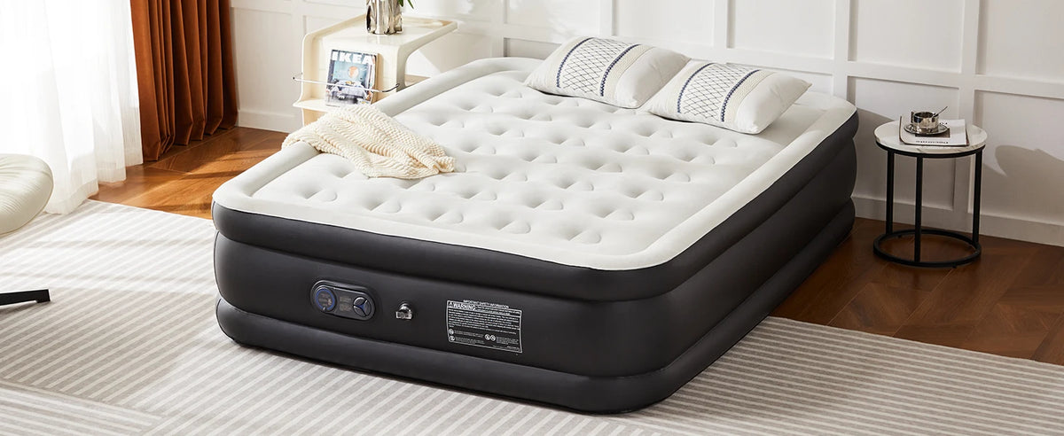 A black air mattress with a white quilted top and a beige towel is placed on a light-colored rug in a room.