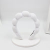 A white sponge terry cloth headband for hair styling displayed on a white circular stand.
