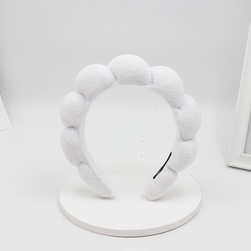 A white sponge terry cloth headband for hair styling displayed on a white circular stand.