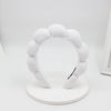 A white sponge terry cloth headband for hair styling displayed on a round white stand.