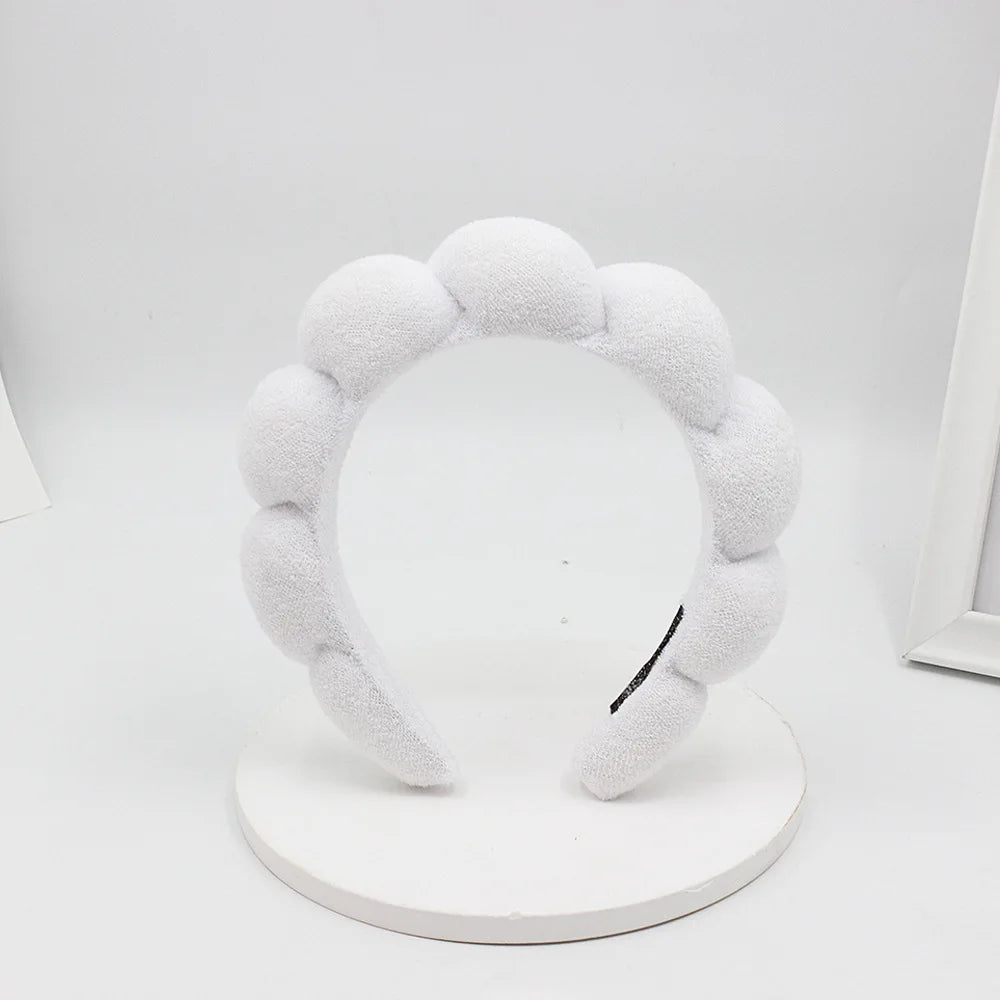A white sponge terry cloth headband for hair styling displayed on a round white stand.