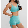 A woman models a teal performance yoga and workout shorts top and bottom set.