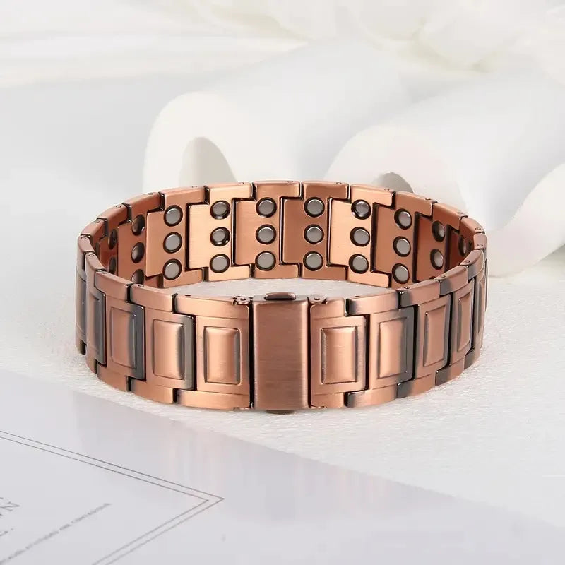 A close-up of a rose gold copper bracelet with magnetic clasps resting on a white surface.