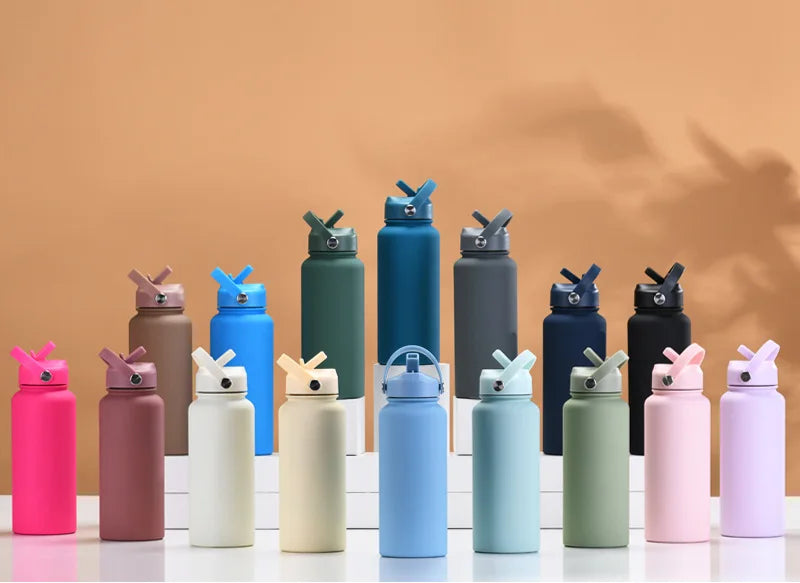 A collection of various colored stainless steel vacuum flasks or water bottles with straws arranged on a white surface.