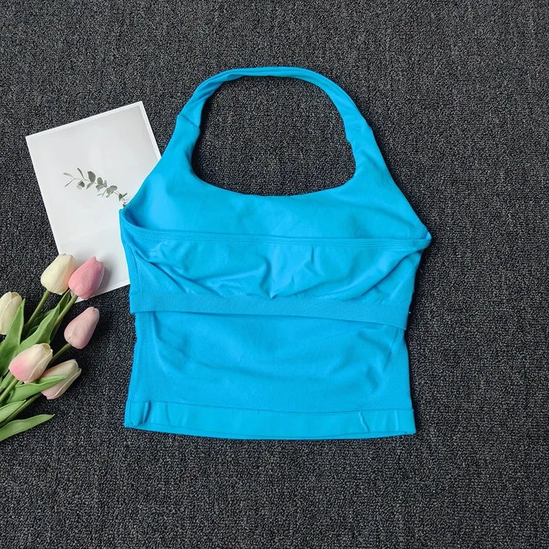 Un haut sans couture bleu vif à bretelles est exposé sur un tissu gris foncé à côté de tulipes roses.