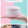 A hand holds a pink and white silicone collapsible coffee cup with a lid against a light background.