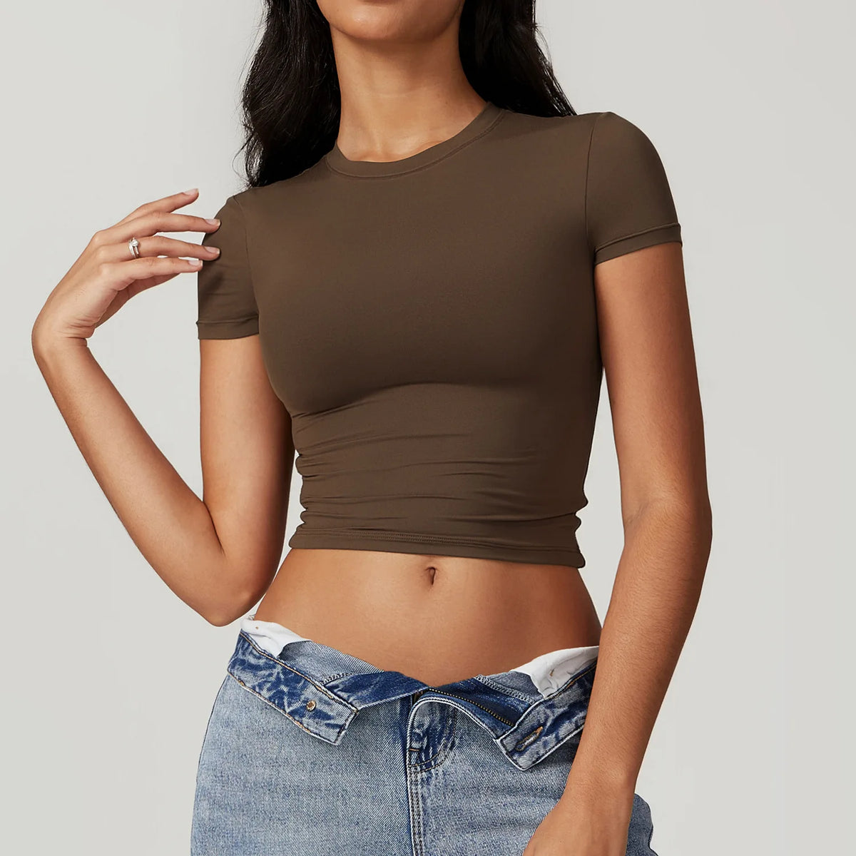 Una modelo vistiendo una camiseta deportiva de yoga y fitness verde oliva oscura y jeans azules.