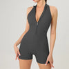 A model wearing a dark gray, sleeveless fitness jumpsuit with a deep V-neck and zipper.