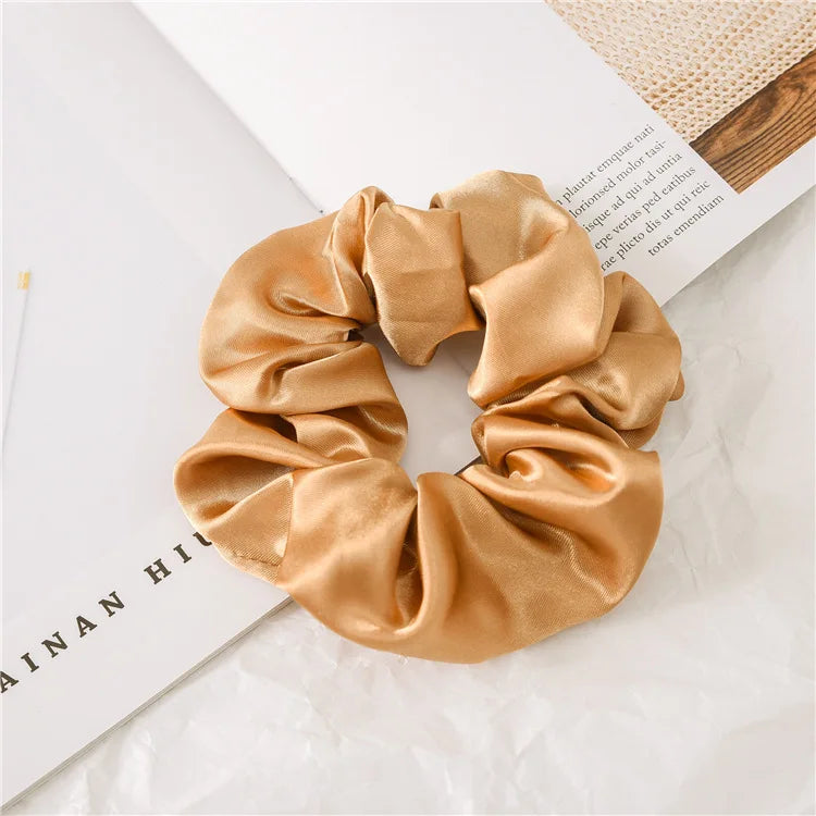 A golden satin scrunchie is shown lying on a white surface next to a book.