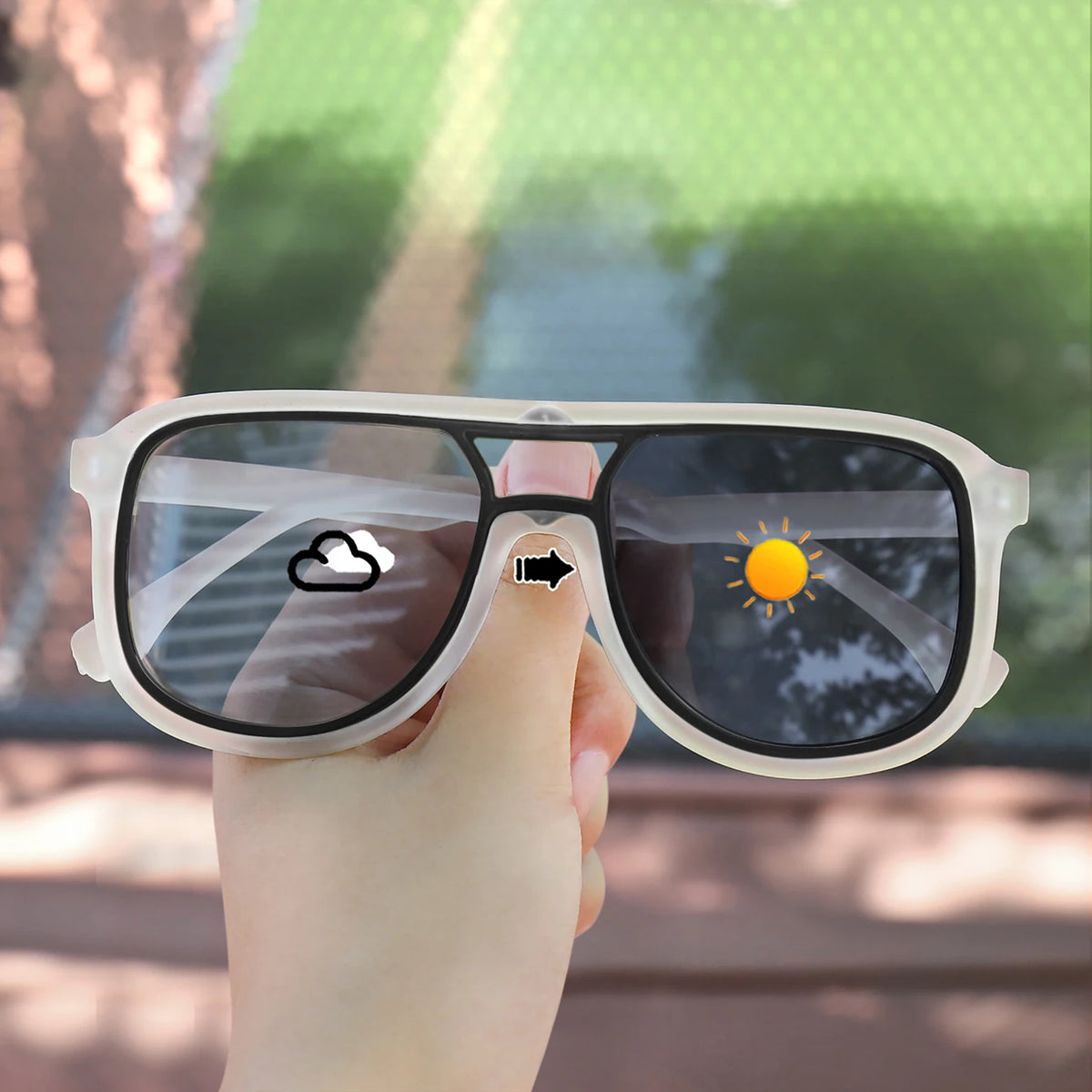A hand holds a pair of clear-lensed photochromic sunglasses with square frames, showing a cloud and a sun icon on the lens.