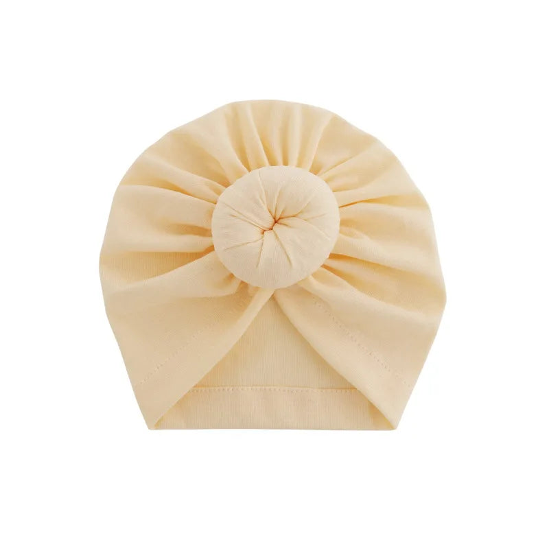 Heller beiger Baumwoll-Baby-Turban, gefaltet in Form einer Blüte.