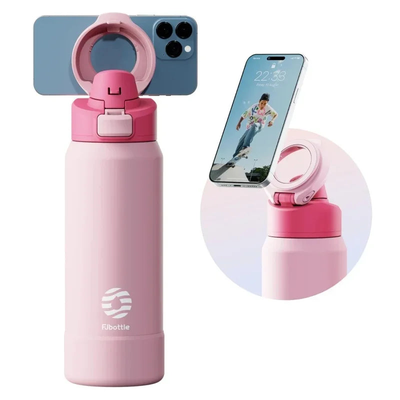 A pink insulated sports water bottle with a magnetic lid and a matching silicone cap, shown next to a smartphone.