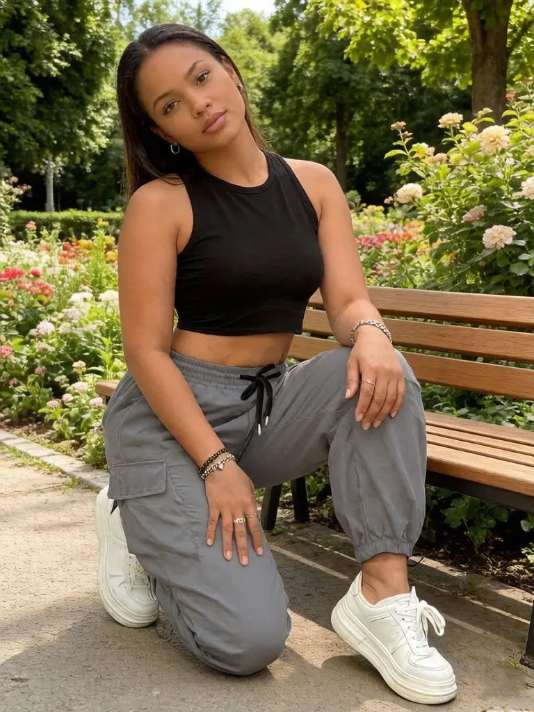 A woman wearing black crop top and gray drawstring cargo joggers sits on a wooden bench outdoors.