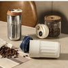 A stainless steel insulated thermos bottle and a white smart display bottle are shown on a table with coffee beans.