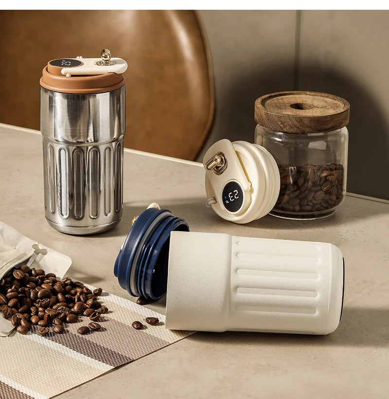A stainless steel insulated thermos bottle and a white smart display bottle are shown on a table with coffee beans.