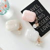 Three cosmetic-style protective cases in pink and white marble with gold charms resting on a black notebook.