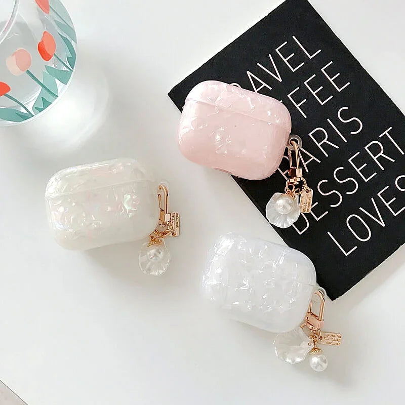 Three cosmetic-style protective cases in pink and white marble with gold charms resting on a black notebook.
