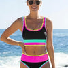 A smiling woman wearing a color-block zigzag three-piece swimsuit set outdoors near the ocean.