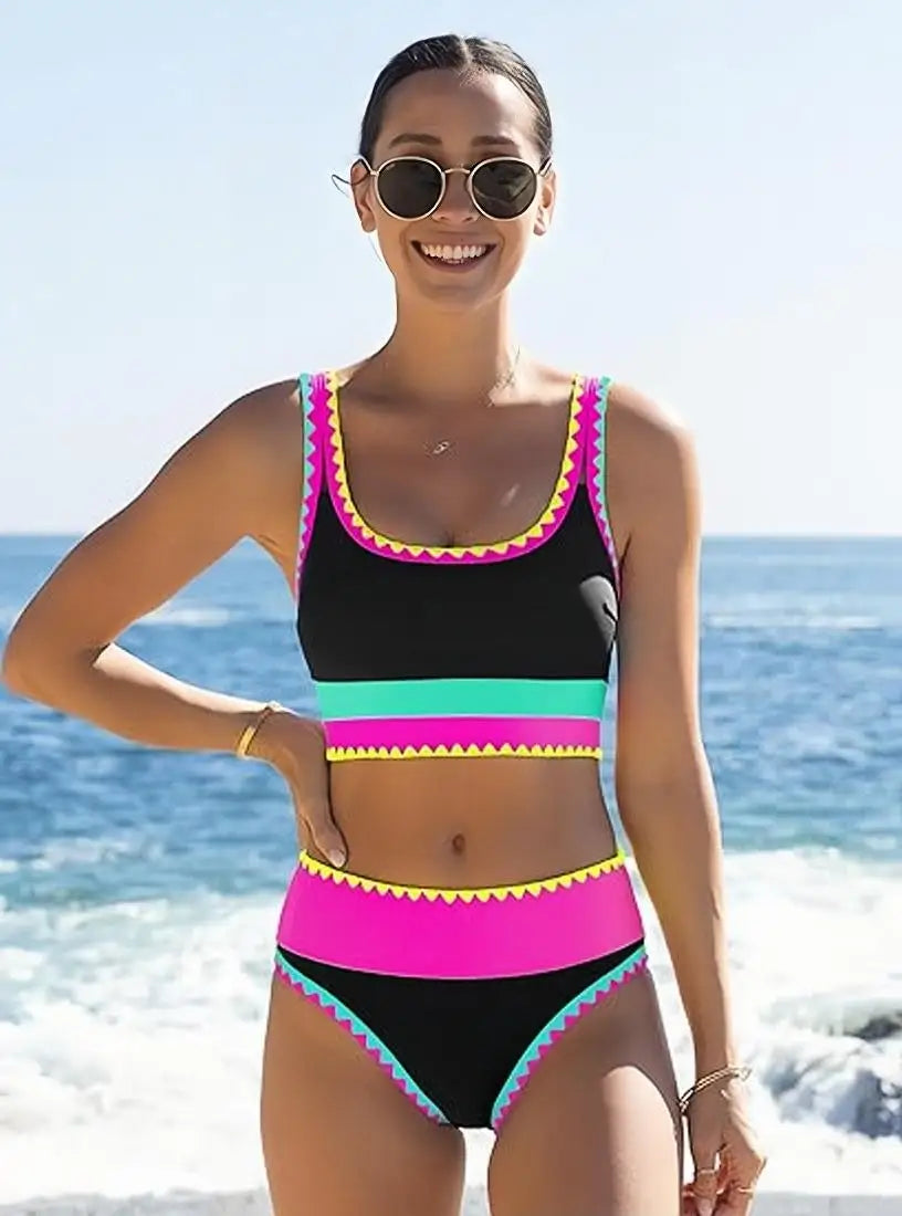 A smiling woman wearing a color-block zigzag three-piece swimsuit set outdoors near the ocean.
