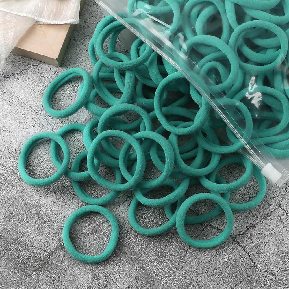 A pile of 50 elastic hair bands in various shades of teal and green coiled inside a clear plastic bag.