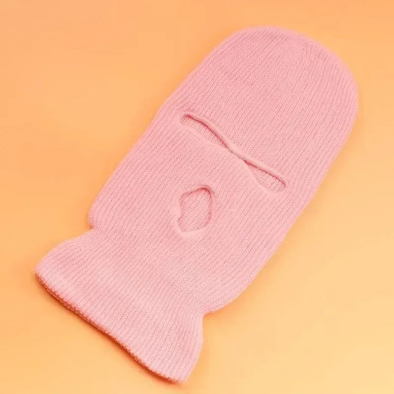 A pink tactical knit balaclava beanie hat lying on an orange background.