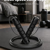 A pair of black speed jump ropes lying on a dark mat with a blurred background showing fitness equipment.