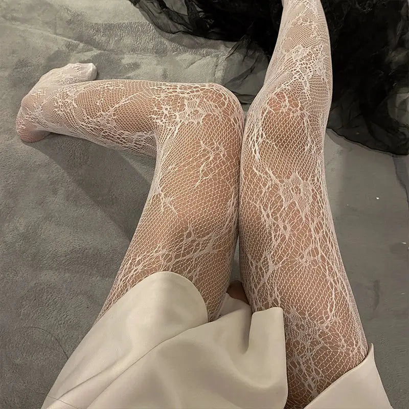 Close-up of sheer floral rattan fishnet hosiery worn on legs, paired with a cream-colored garment.