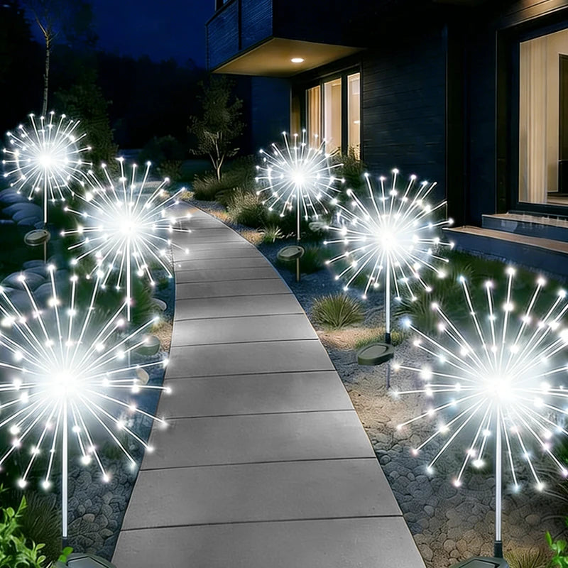 Un sendero iluminado por numerosas luces de hadas en forma de estrella blanca decorando un jardín al aire libre por la noche.