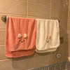 A pink coral fleece face towel hanging on a tiled wall next to a white towel.