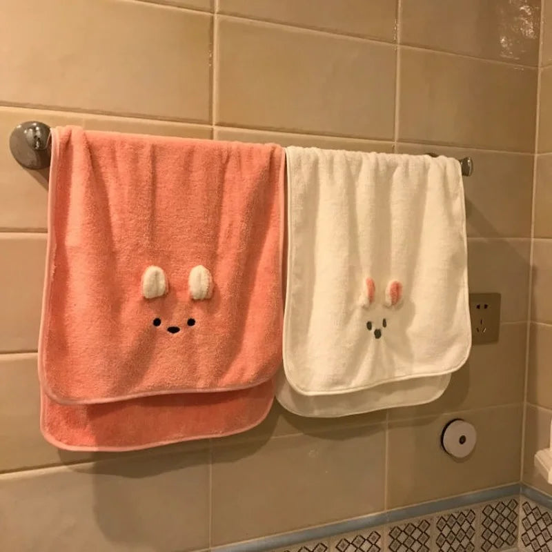 A pink coral fleece face towel hanging on a tiled wall next to a white towel.