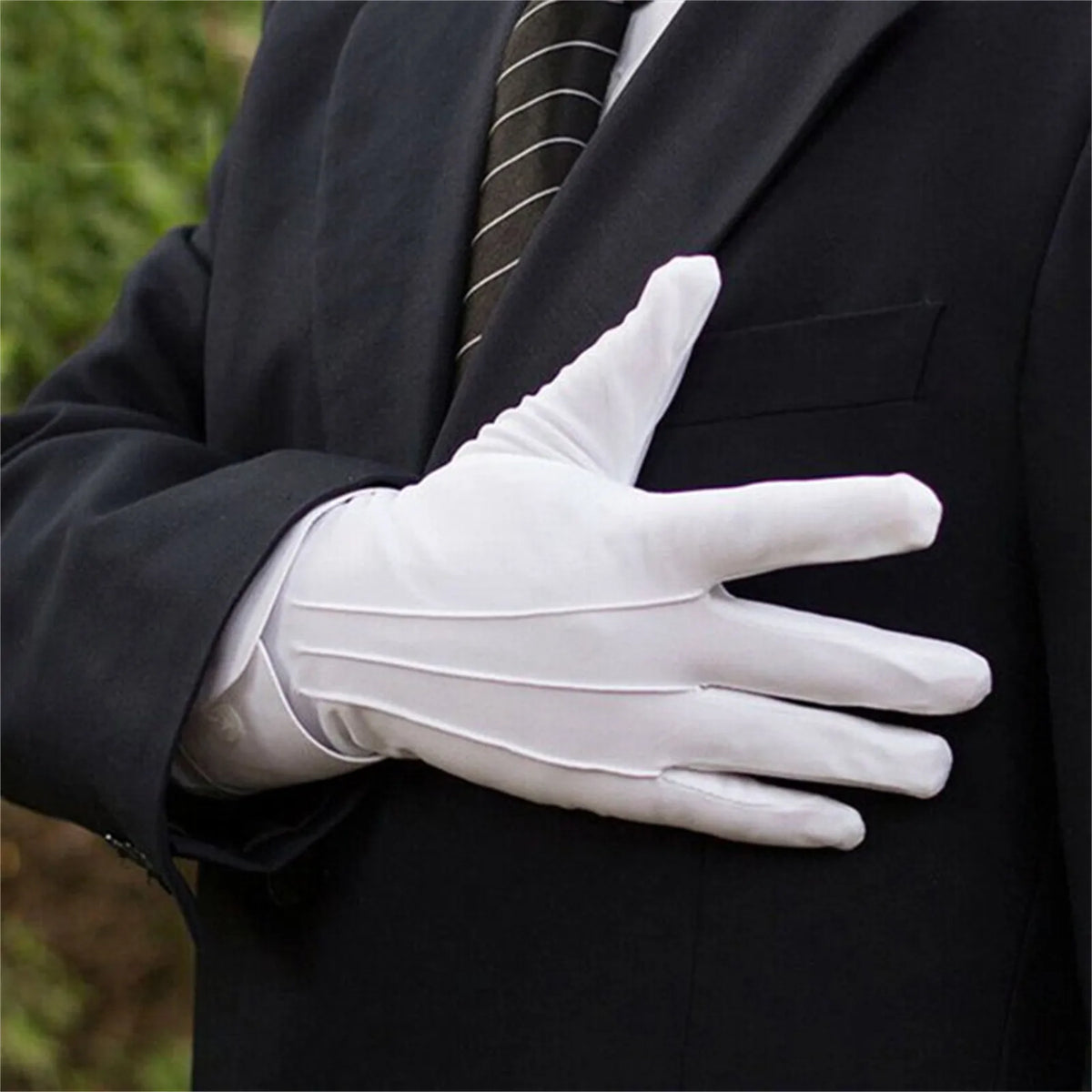 Una persona con chaqueta de traje negra sostiene un guante de algodón blanco con la mano extendida.
