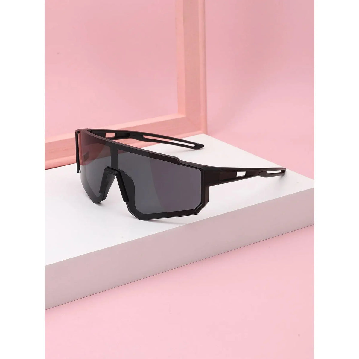 A pair of black sports sunglasses resting on a white surface against a pink background.