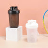 A dark brown portable protein shaker bottle with a black cap and a clear white shaker cup is displayed on a light surface.